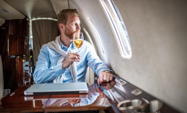 Image of a rich man on a plane drinking a glass of wine.