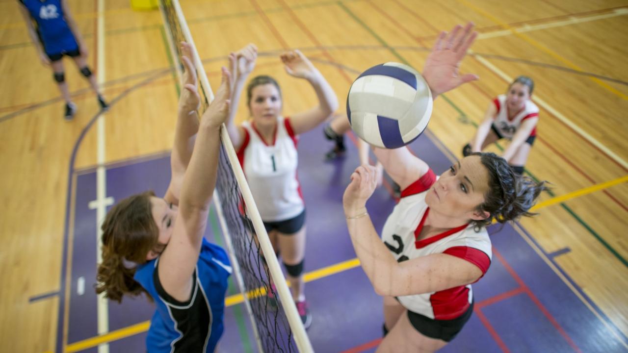 Aerial view from the top of a volleyball net showing two women jumping up to spike the ball