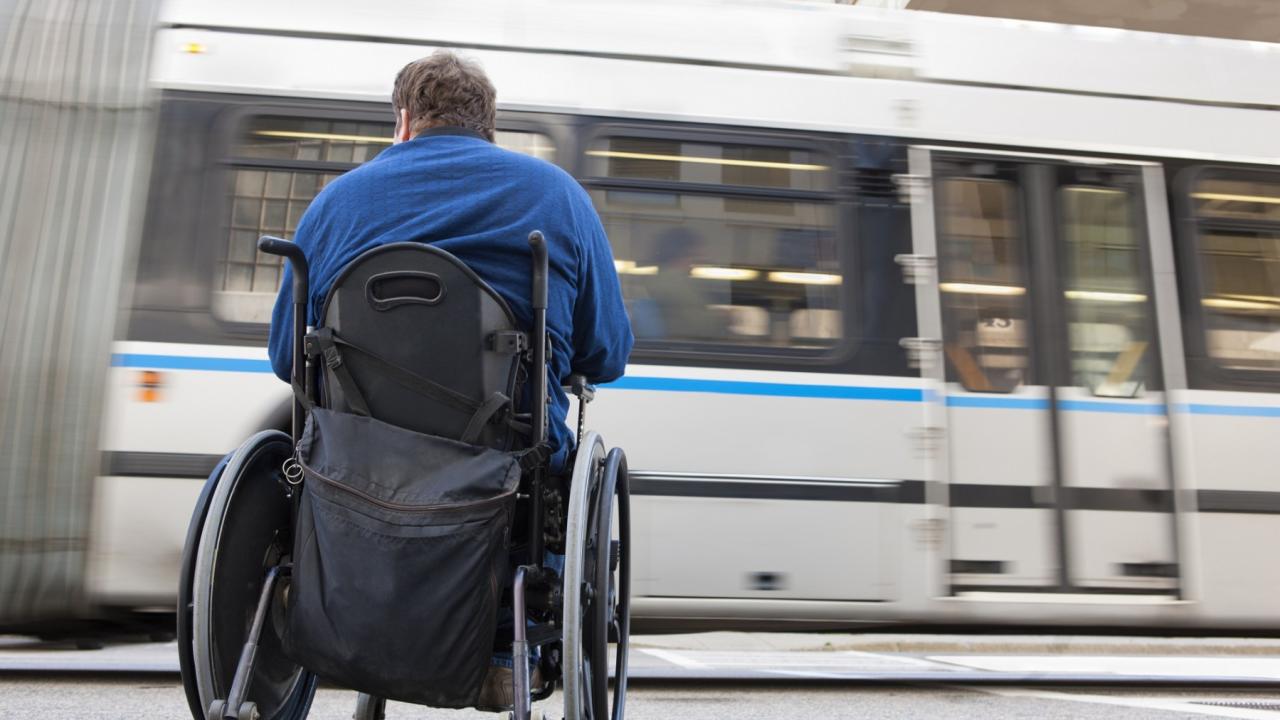 A man in a wheelchair is facing a moving train on a railway platform