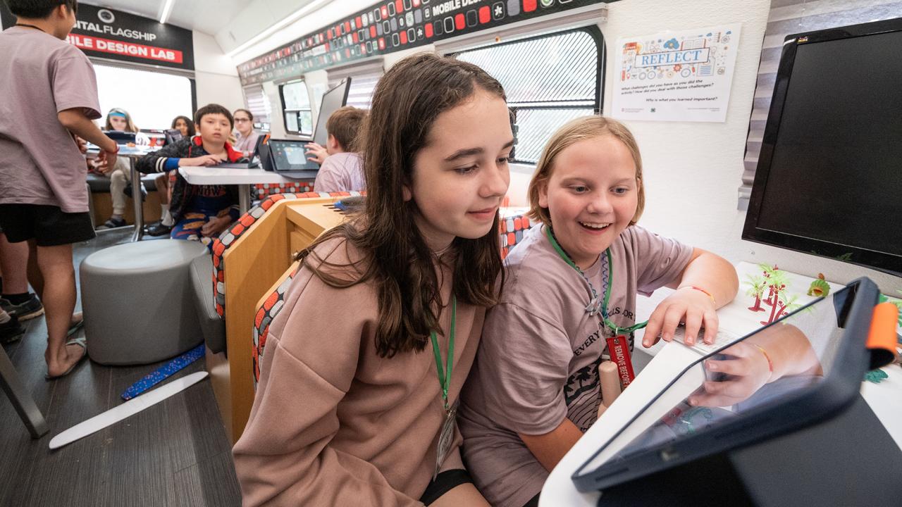 Two girls look at a tablet while sitting in the 4-H Mobile Design Classroom.